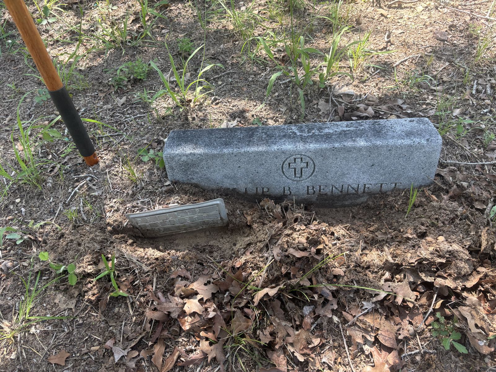 A partially buried cemetery headstone surrounded by soil and fallen leaves